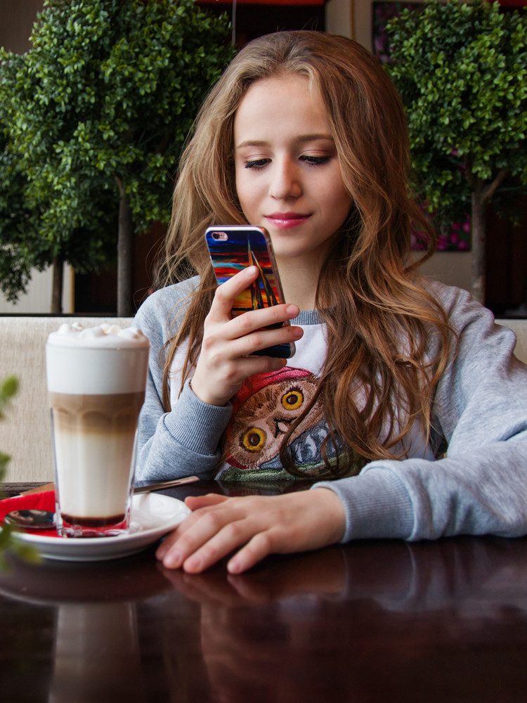 Young woman looking at cellphone drinking coffee