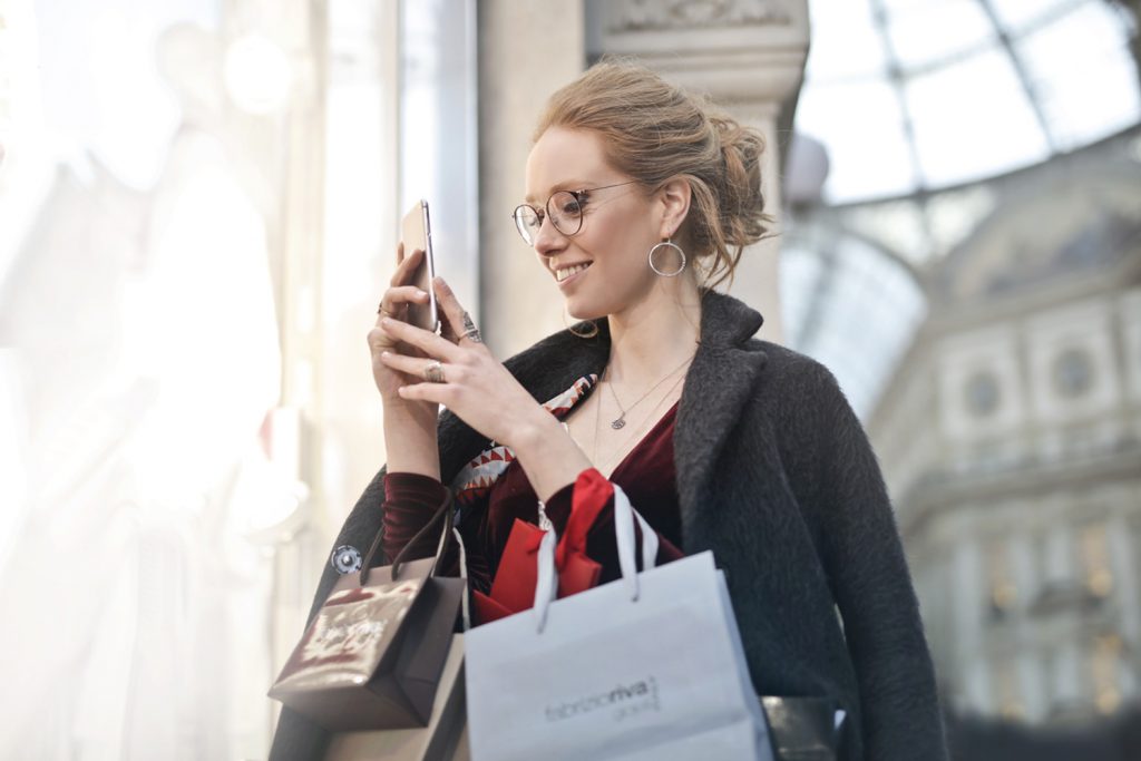 Woman looking at cellphone happy with shopping bags