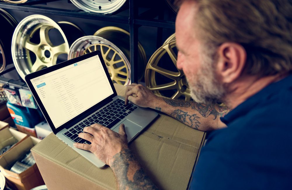 Man on laptop with car rims in background