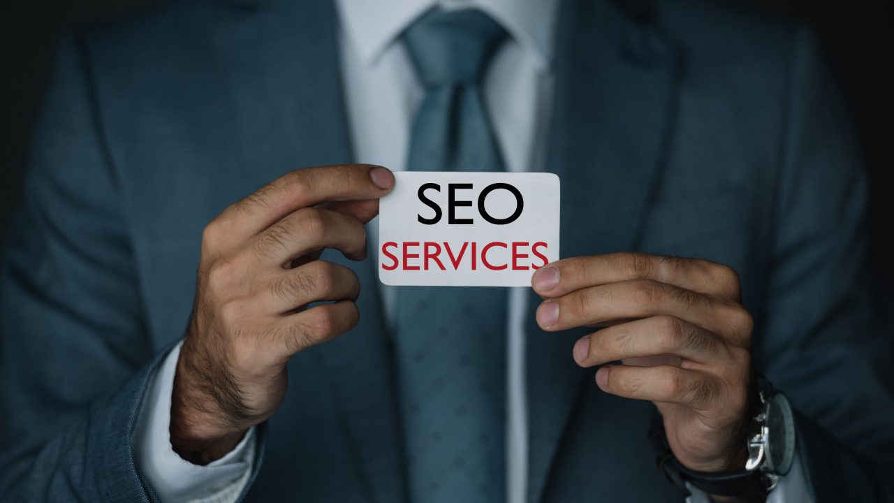cropped view of SEO specialist in suit holding business card with SEO services