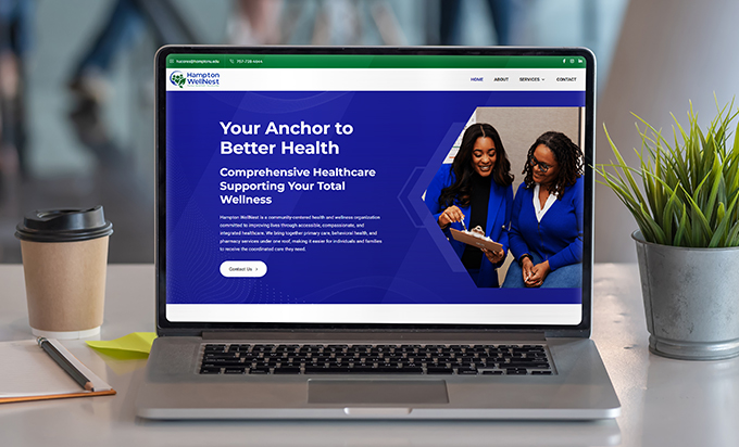 A laptop on a desk displays the Hampton WellNest healthcare website with two smiling women in blue blazers on the homepage.